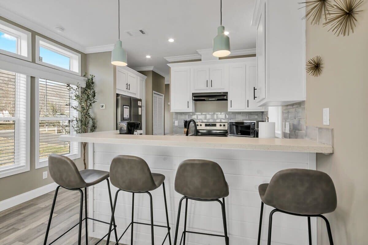 A modern kitchen with white cabinets, a large island with bar stools, pendant lighting, and a view of the outdoors.