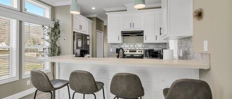 A modern kitchen with white cabinets, a large island with bar stools, pendant lighting, and a view of the outdoors.