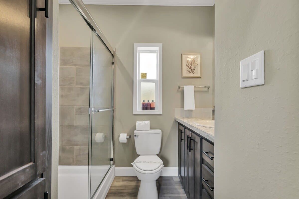 A bathroom with a glass shower enclosure, a toilet, and a sink with a countertop.