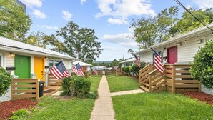 A row of mobile homes with American flags, a central pathway, and a green door on the left. - 12th Ave The Bricks - Unit 4 (Birmingham)
