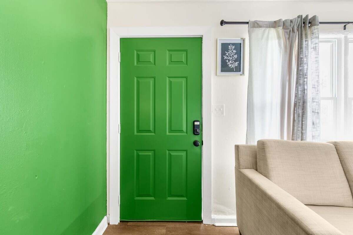 Une pièce avec une porte verte, un canapé beige et un tableau encadré accroché au mur.