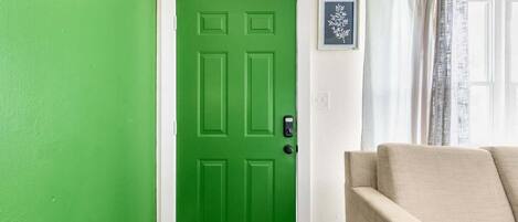 Une pièce avec une porte verte, un canapé beige et un tableau encadré accroché au mur.