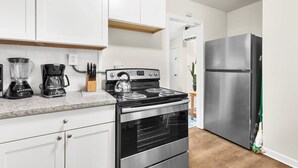 A modern kitchen with white cabinets, a stainless steel refrigerator, a stove, and a coffee maker. - 12th Ave The Bricks - Unit 4 (Birmingham)