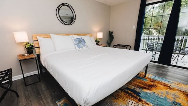 Une chambre avec un grand lit, deux tables de chevet avec des lampes, un miroir au mur et une vue sur le balcon extérieur.