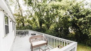 Une terrasse extérieure couverte, aménagée avec des meubles en osier et une table en verre, et entourée d’une végétation luxuriante.
