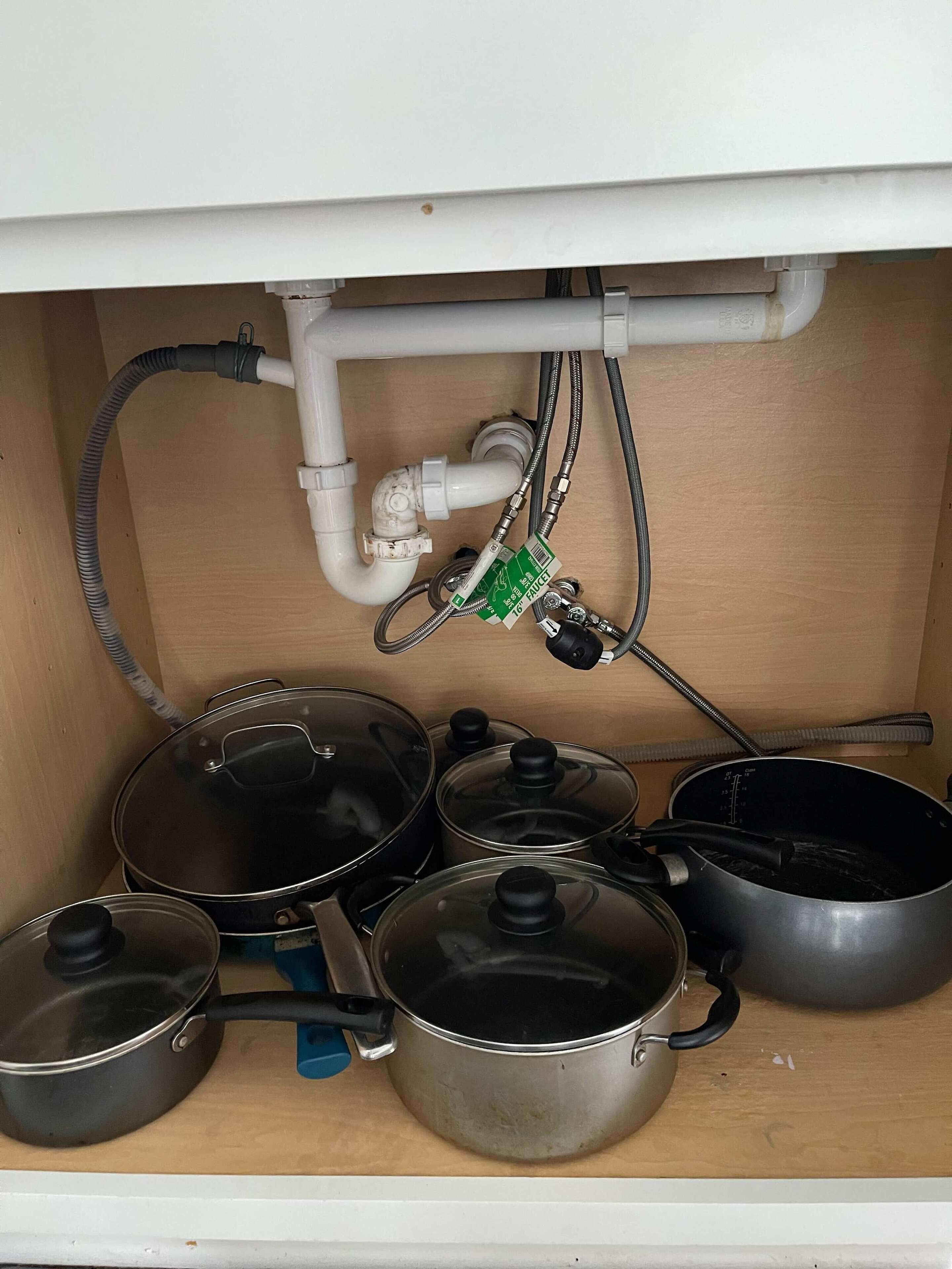A kitchen with pots and pans stored under a cabinet, a water filter, and a faucet.