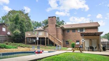 A two-story brick house with a deck, a swimming pool, and outdoor seating.