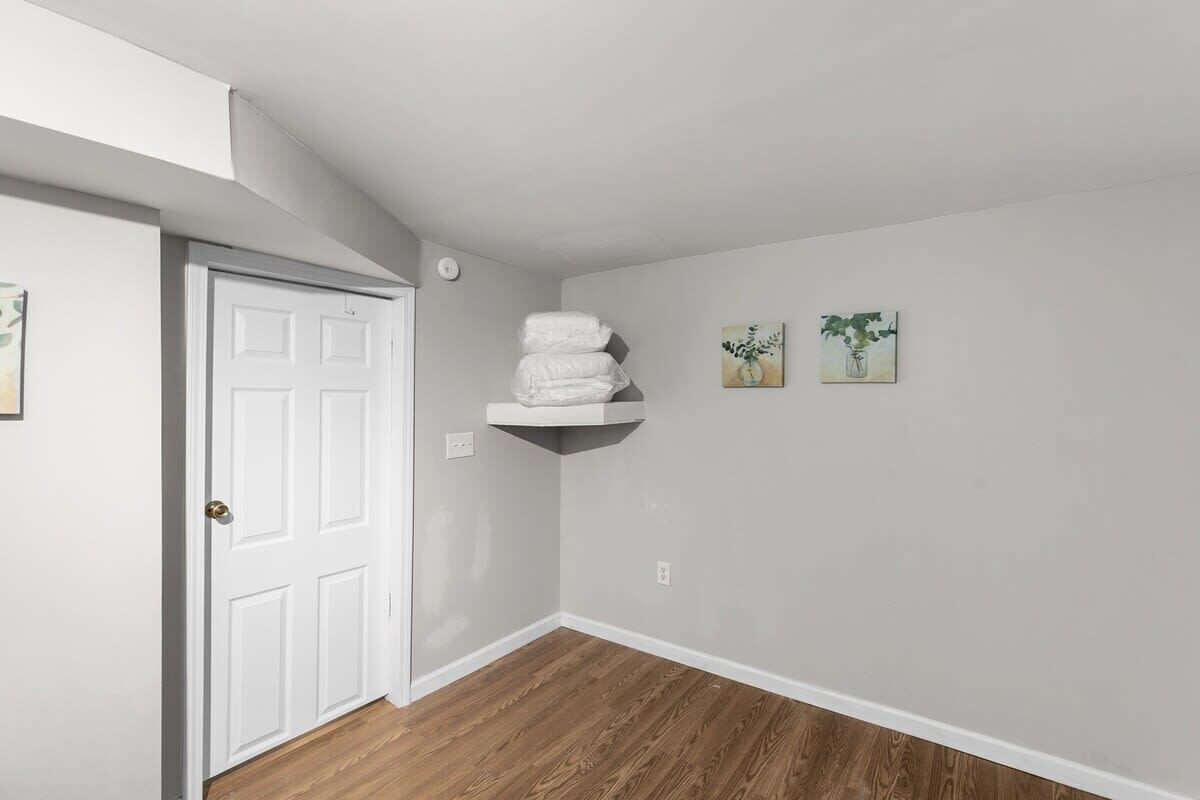 A hallway with a white door, a wooden floor, and a white shelf with folded towels.