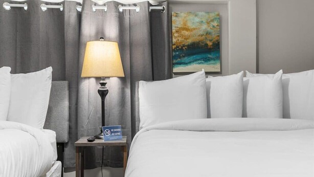 Een hotelkamer met een bed, nachtkastje met een lamp, een rookverbod bord en een schilderij aan de muur.