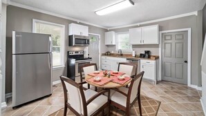 A modern kitchen with white cabinets, a stainless steel refrigerator, a microwave, and a stove. There is a dining table with chairs and a rug. - Bradley Blissful (Huntsville)