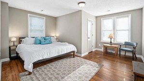 A bedroom with a bed, a nightstand, a chair, and a small table with a lamp. - Bradley Blissful (Huntsville)
