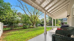A covered porch with wicker furniture, a concrete pathway, and a grassy yard with trees. - Bradley Blissful (Huntsville)