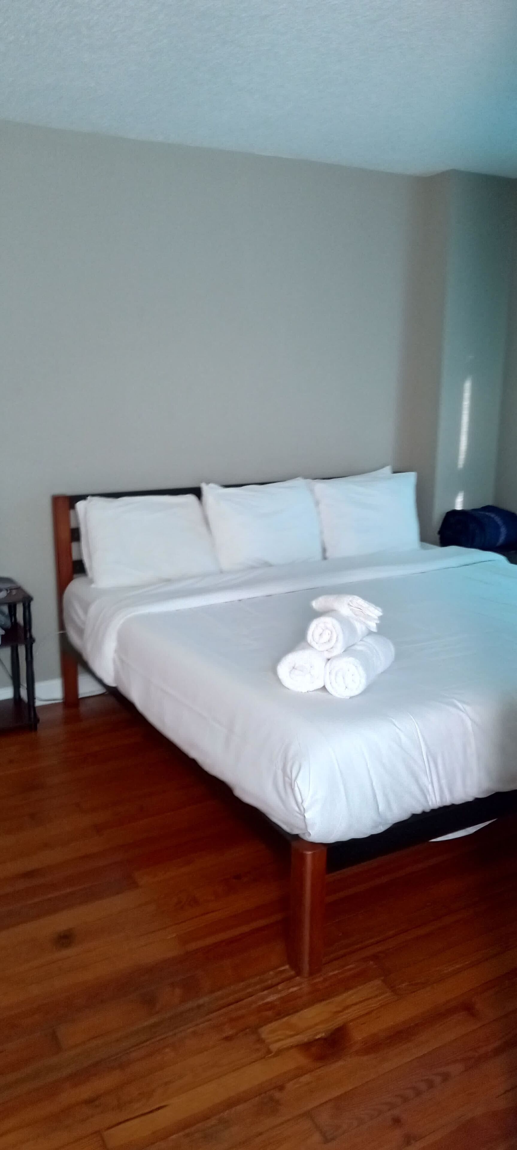 A neatly made bed with white linens and rolled towels on the bed.