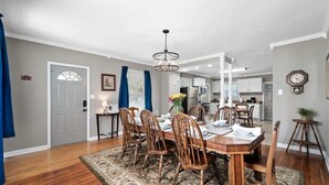 A dining room with a wooden table and chairs, a chandelier, and a kitchen in the background. - Bradley Blissful (Huntsville)