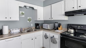 Een moderne keuken met witte kasten, een zwarte oven, een magnetron en een koffiezetapparaat.