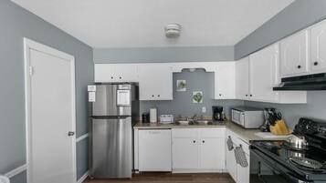 Cocina compacta con armarios blancos, refrigerador de acero inoxidable, microondas, estufa y lavavajillas.