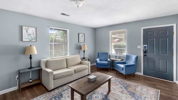 Een woonkamer met een beige bank, blauwe fauteuils, een salontafel en een tapis met een patroon.