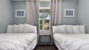 Een slaapkamer met twee eenpersoonsbedden, een raam met gordijnen, een nachtkastje met lamp en ingelijste foto's aan de muur.