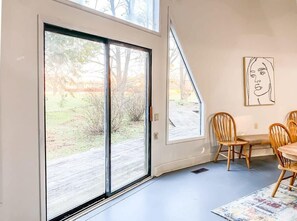 A room with a large sliding glass door leading to a garden, a dining area with wooden chairs, and a wall-mounted artwork. - Bell Circle Eccentric Geodesic Dome-home (Huntsville)
