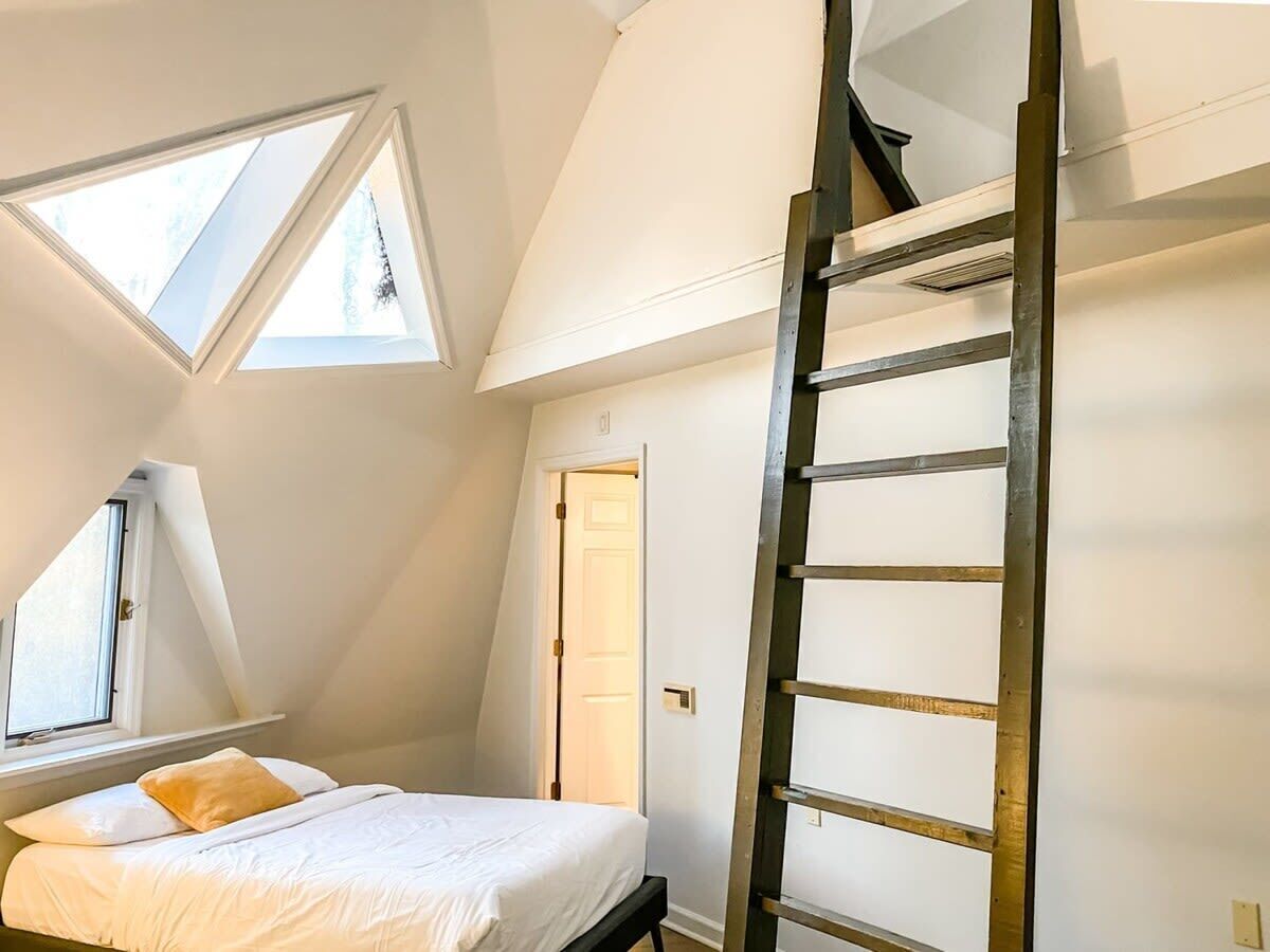 A bedroom with a loft bed, skylights, and a wooden ladder.
