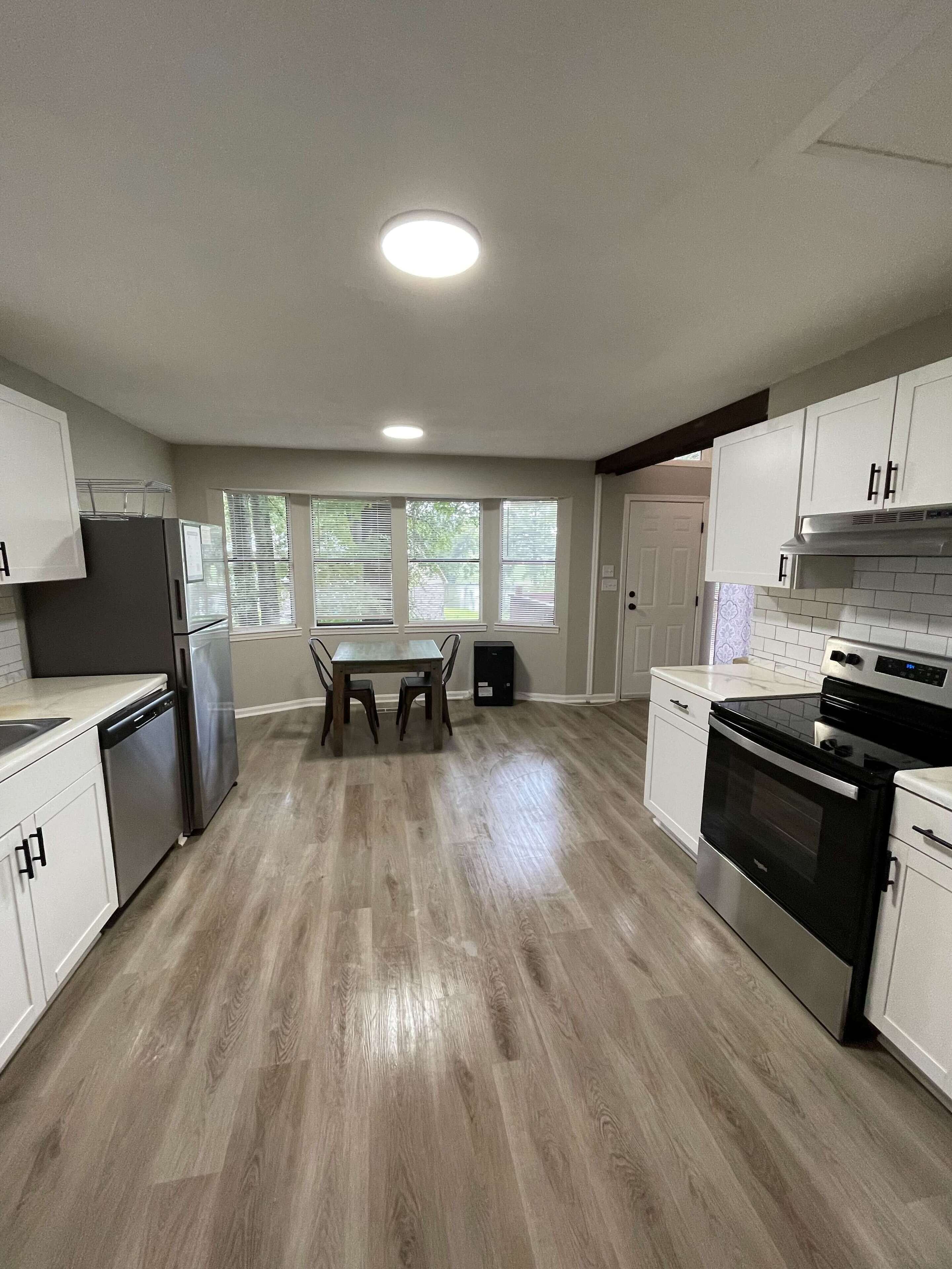 A modern kitchen with white cabinets, a stainless steel refrigerator, a black oven, and a dining table with chairs.