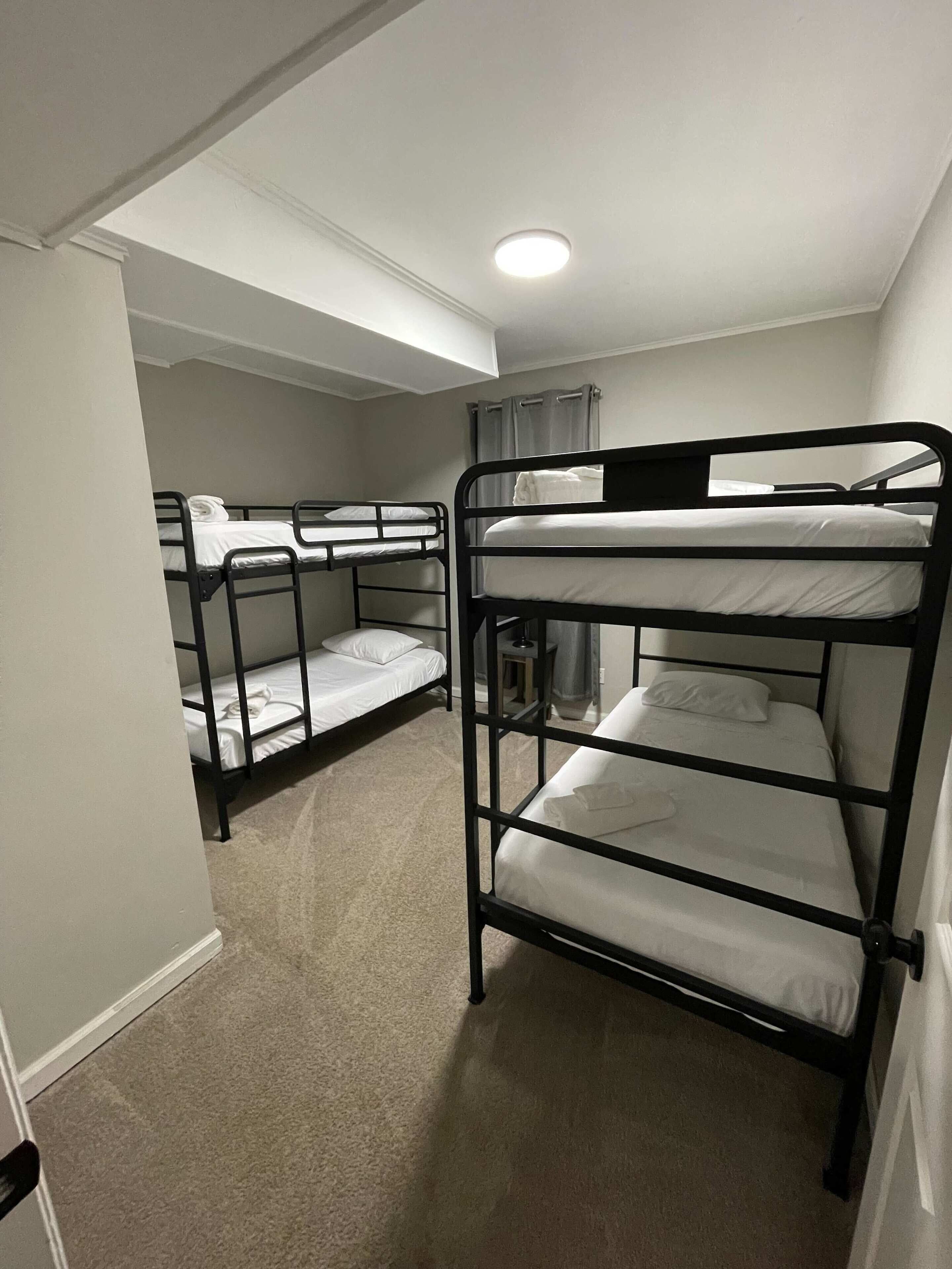 A room with three bunk beds, a ceiling light, and a window with curtains.