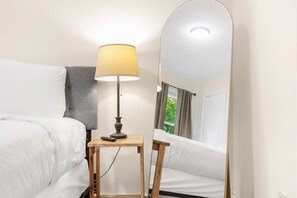 A hotel room with a bed, a bedside table with a lamp, and a large mirror.