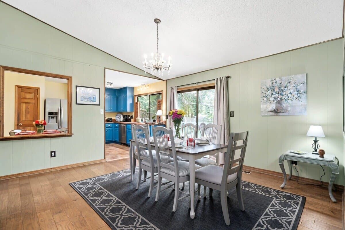 Spiseområde med en lysekrone, et bord med stole, et tæppe og et maleri på væggen.