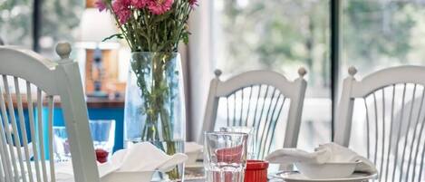 Una mesa de comedor con sillas blancas, un jarrón de flores y un vaso de agua.