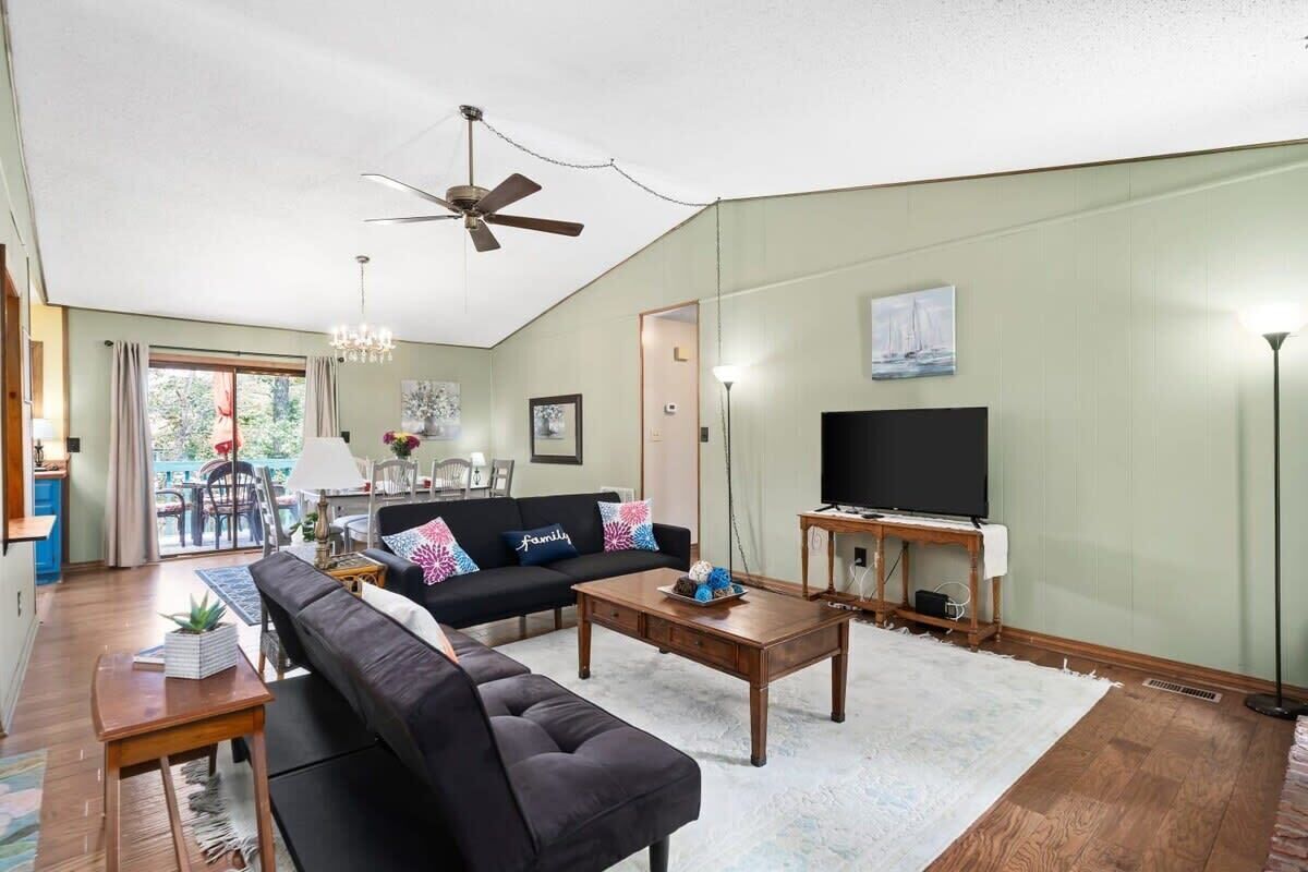 Un salon avec un canapé, une table basse et un téléviseur. On y trouve un ventilateur de plafond, un lustre et un tableau au mur.