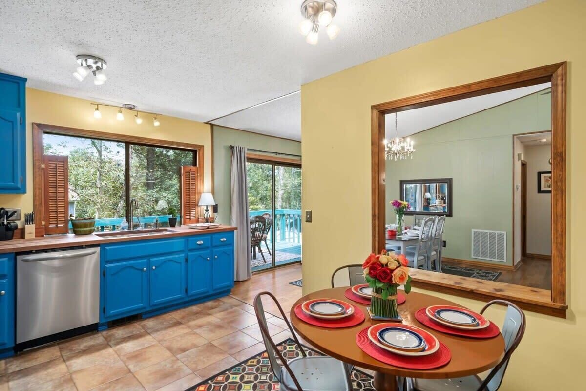 A dining area with a round table set for four, a kitchen with blue cabinets, and a large mirror reflecting the dining area.