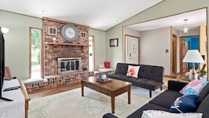 A living room with a brick fireplace, a black sofa, a wooden coffee table, and a television on a stand. - Eastview Drive Jolly Green Giant (Madison)