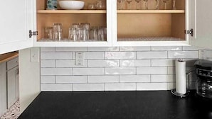 A kitchen with white cabinets, a black countertop, and a tiled backsplash. - 28th Street Historic at Norwood (Birmingham)