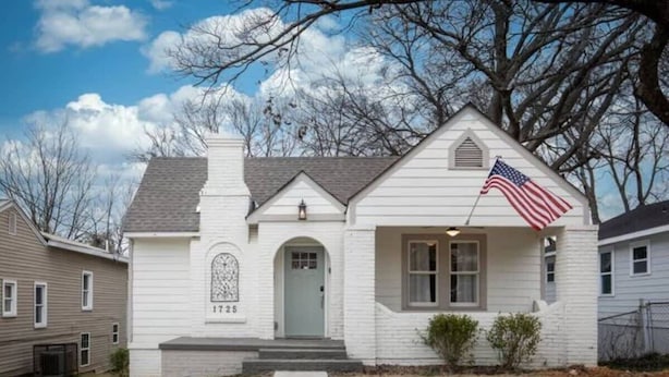 A white single-story house with a front porch, a small front yard, and an American flag. - 28th Street Historic at Norwood (Birmingham)