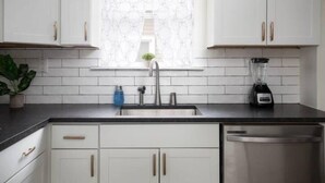 A modern kitchen with white cabinets, a black countertop, a stainless steel sink, and a dishwasher. - 28th Street Historic at Norwood (Birmingham)