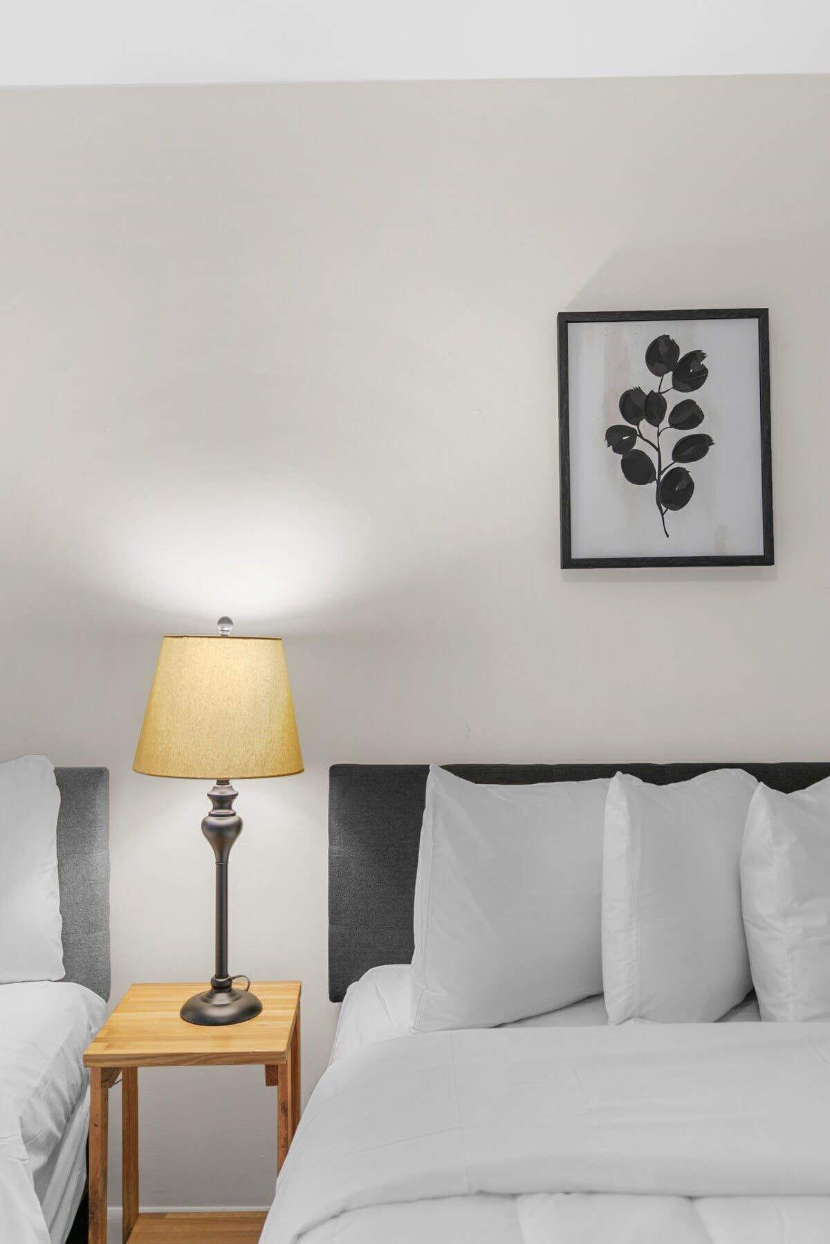 A hotel room with a bed, a bedside table with a lamp, and a framed botanical print on the wall.