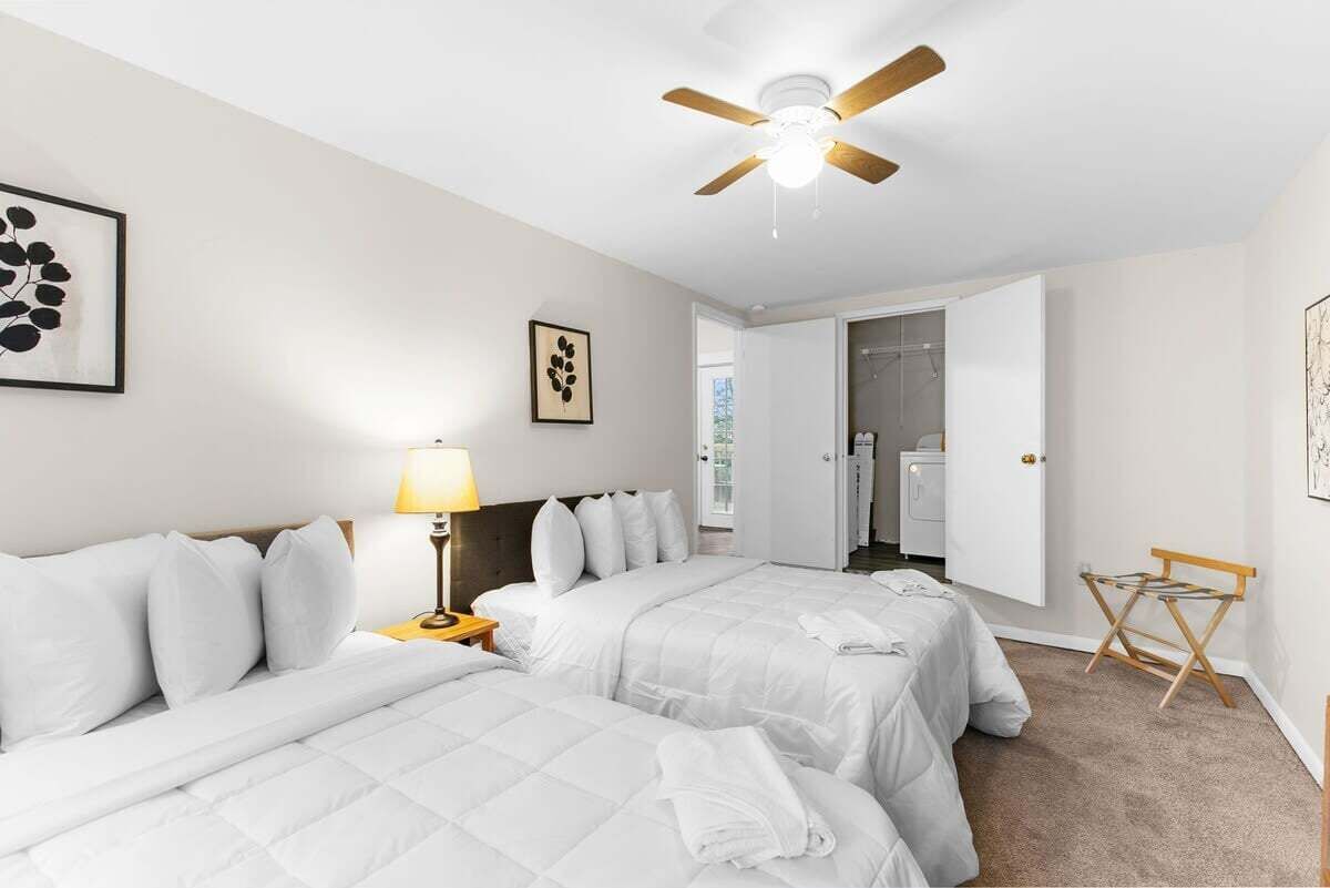 Habitación de hotel con dos camas, ventilador de techo, lámpara y cuadros en las paredes.