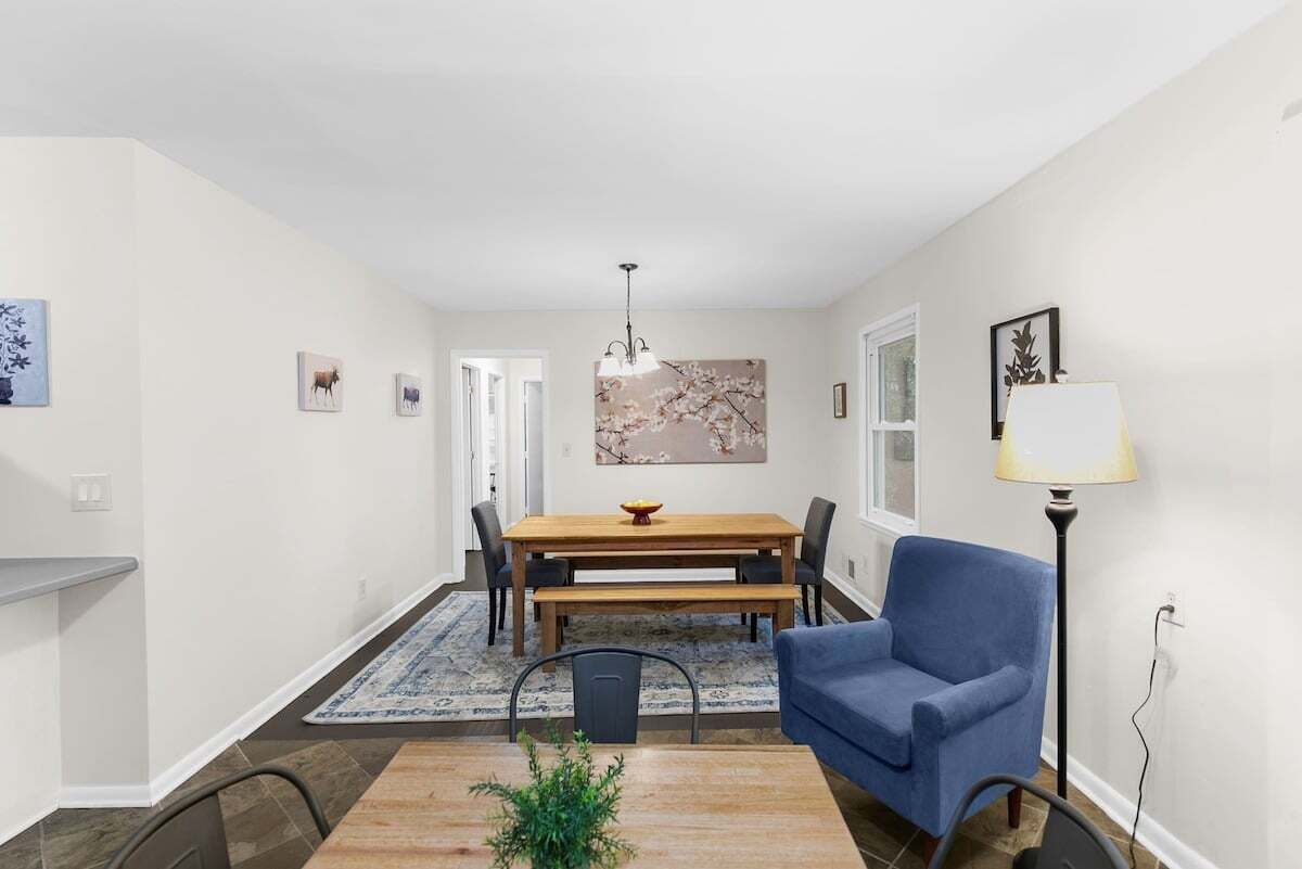 A dining area with a wooden table and chairs, a blue armchair, a floor lamp, and a rug.