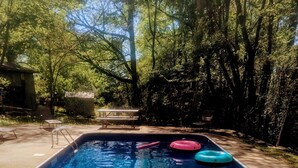 Une piscine rectangulaire à l’eau d’un bleu cristallin, entourée d’arbres et bordée d’une terrasse en béton.
