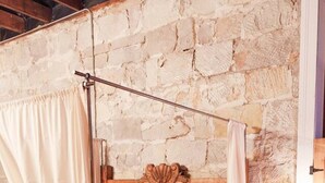 Une chambre à coucher rustique avec un mur en pierre, un lit en bois surmonté d’un baldaquin, un tapis en fourrure et une table de chevet en bois.