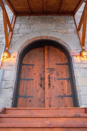 Una porta d'arc de fusta amb un mosquetó metàl·lic, flanquejada per parets de pedra i bigues de fusta, sota un porxo cobert.