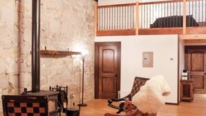 A rustic interior with exposed wooden beams, a fireplace, a checkered chair, and a fluffy dog. - The Scandinavian West Hall—Near Anthony Lakes! (North Powder)