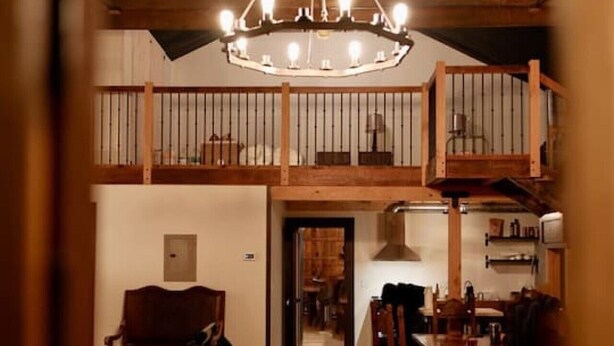 A spacious interior with a high ceiling, a chandelier, wooden beams, and a staircase leading to an upper level. - The Scandinavian West Hall—Near Anthony Lakes! (North Powder)