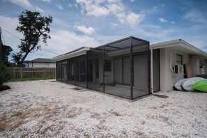 A modern house with a covered patio area, a gravel driveway, and a tree in the background.