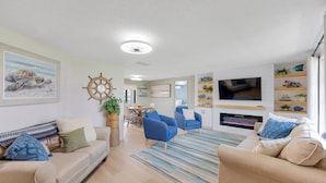 A modern living room with a beige sofa, blue armchairs, a striped rug, a wall-mounted TV, and a fireplace. - Coastal Oasis ~  Beaches, Parks, Shopping & Entertainment, Pet Friendly (Venice)