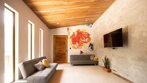 Una sala de estar moderna con un sofá gris, techo de madera, un cuadro grande y un televisor montado en la pared.