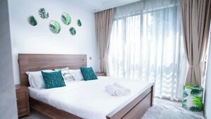 Ein ordentlich bezogenes Bett mit hölzernem Kopfteil, weißer Bettwäsche und einem grünen Kopfkissen.
