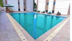 Ein Schwimmbecken mit Fliesen umgeben, umgeben von einem Gebäude mit mehreren Fenstern und einer flachen Dachterrasse.