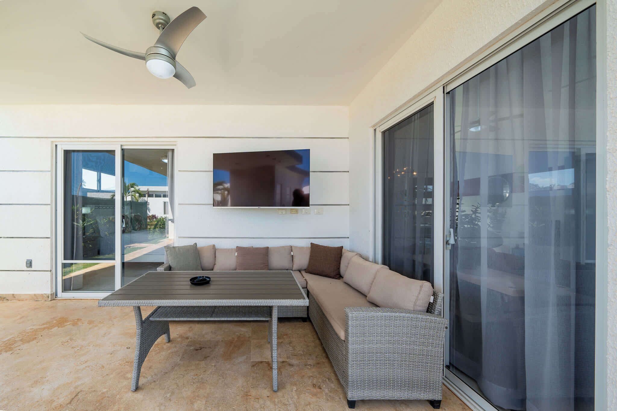 A modern outdoor living area with a ceiling fan, a sofa, a table, and a sliding glass door.