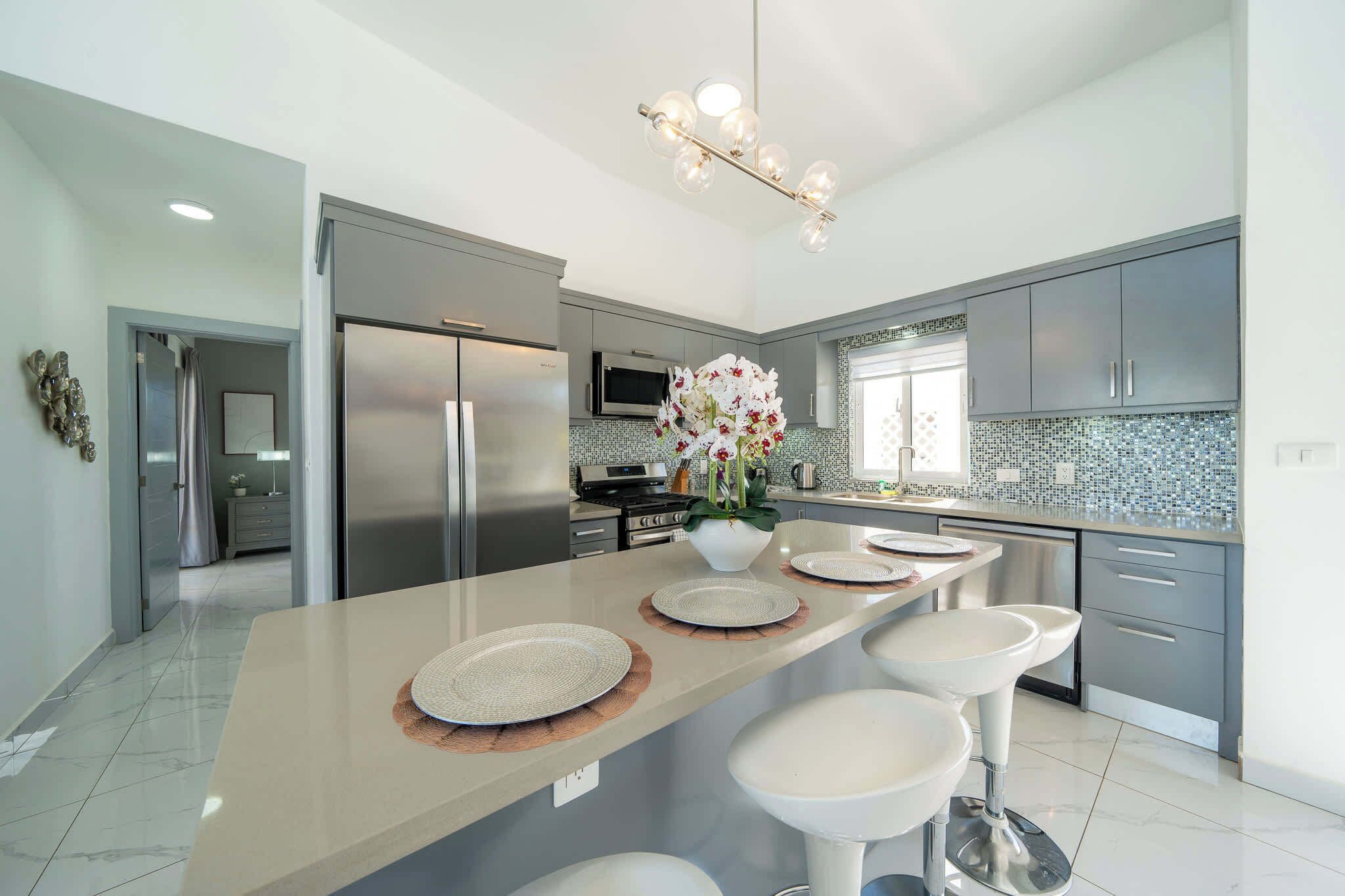 A modern kitchen with a central island, stainless steel appliances, and a tiled backsplash.